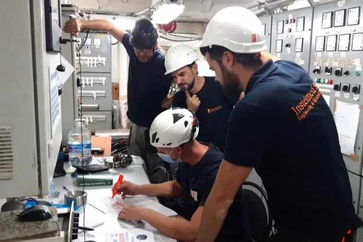 Equipo de Insteimed con casco revisando planos frente a un cuadro eléctrico a bordo