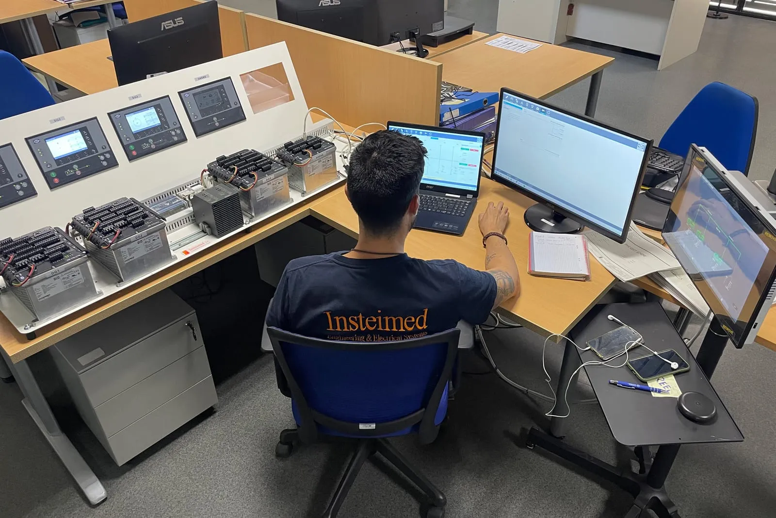 Técnico de Insteimed trabajando con esquemas eléctricos en varias pantallas en la oficina técnica